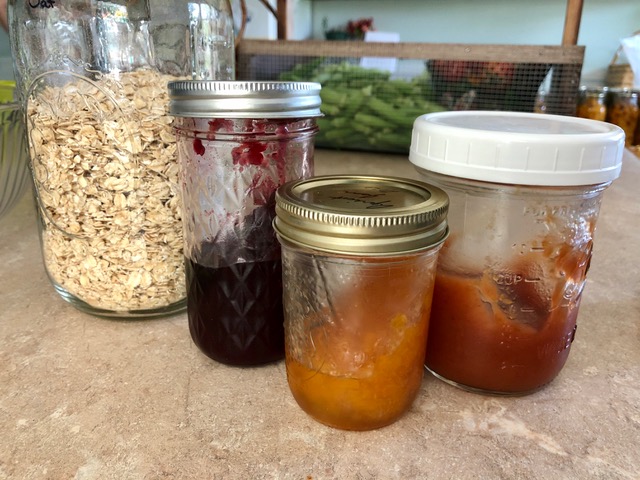 Mason jars of rolled oats and various flavors of jam sitting on the counter.