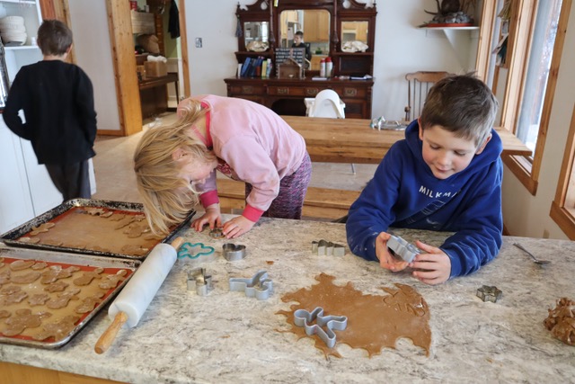 Kids cutting out gingerbread shapes from dough on the counter.