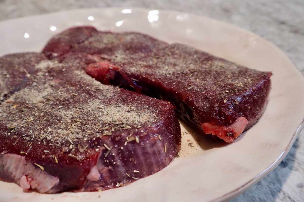 To raw venison steaks resting on a plate.