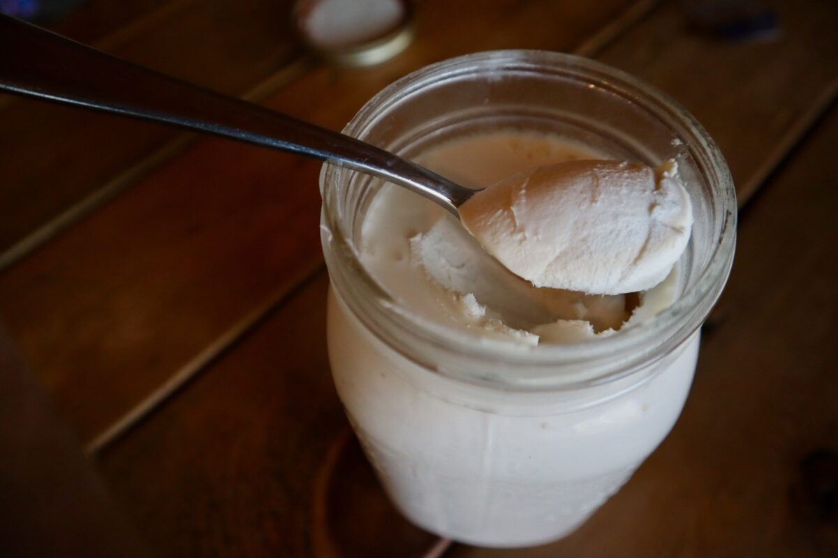 A spoon pulling out a scoop of homemade sour cream from a mason jar.