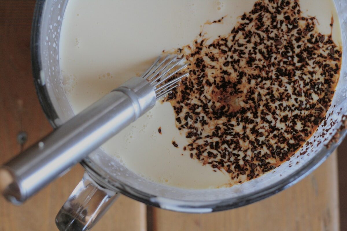 A whisk in a measuring cup of milk with instant coffee granules.