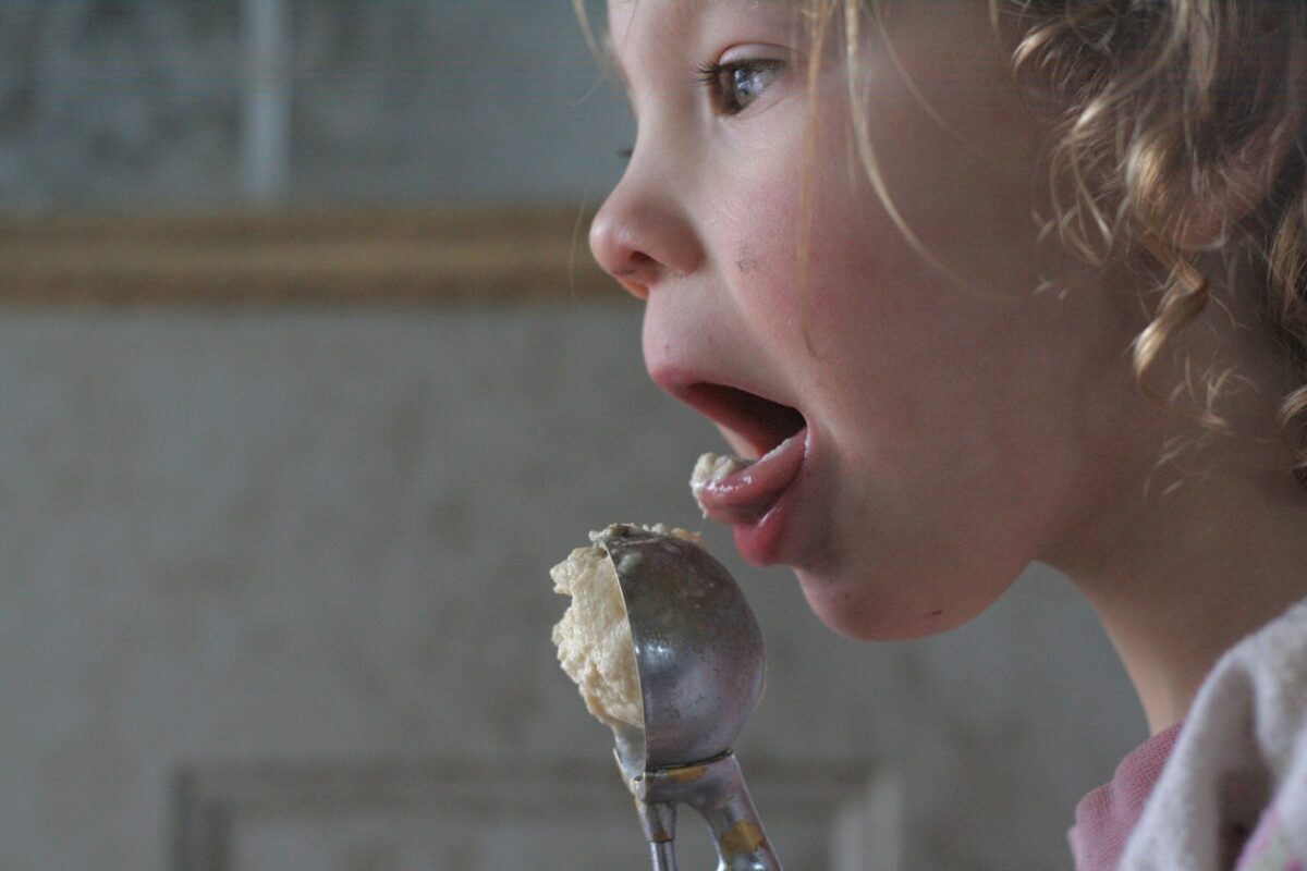 Small girl licking coffee ice cream off a metal scoop.