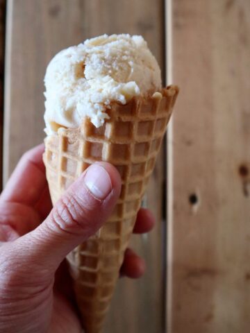 Hand holding an ice cream cone in front of a wooden slat wall.