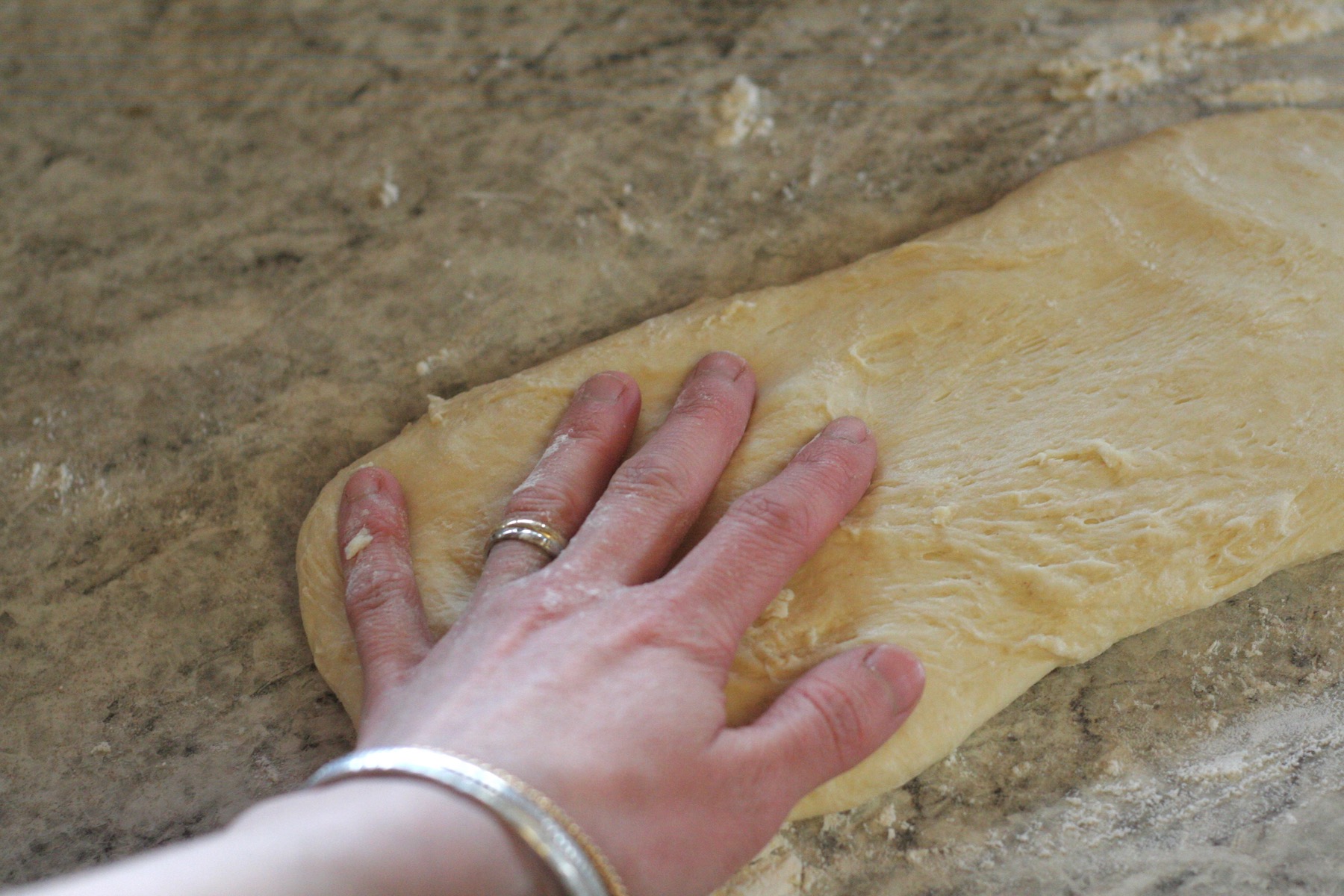 A hand showing the size of a French bread rectangle on a floured counter.
