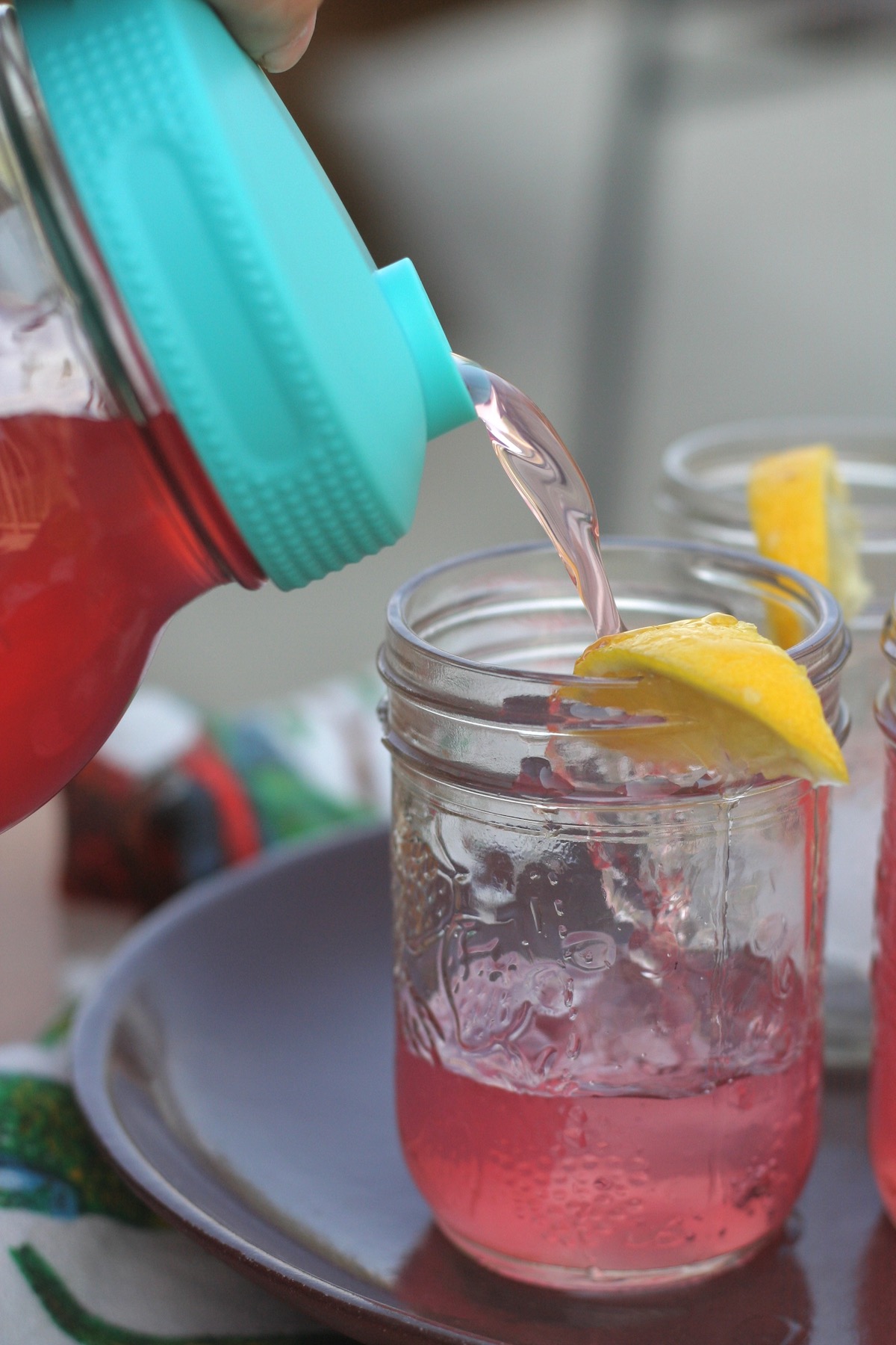 Pouring herbal iced tea from a large mason jar to pint jars.