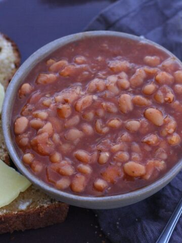 Vegan maple baked beans in a bowl next to buttered bread.