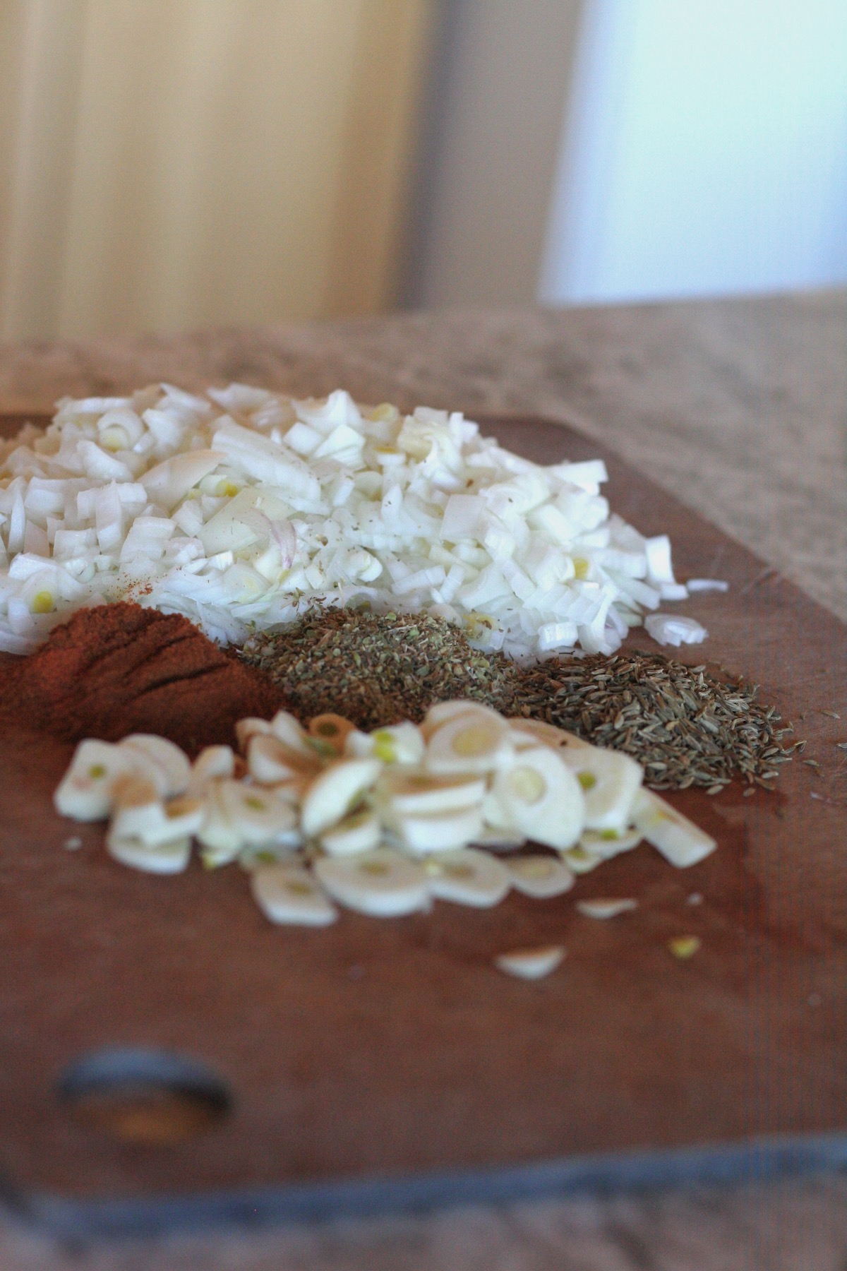 Chopped onions and garlic with spices on a wooden cutting board.