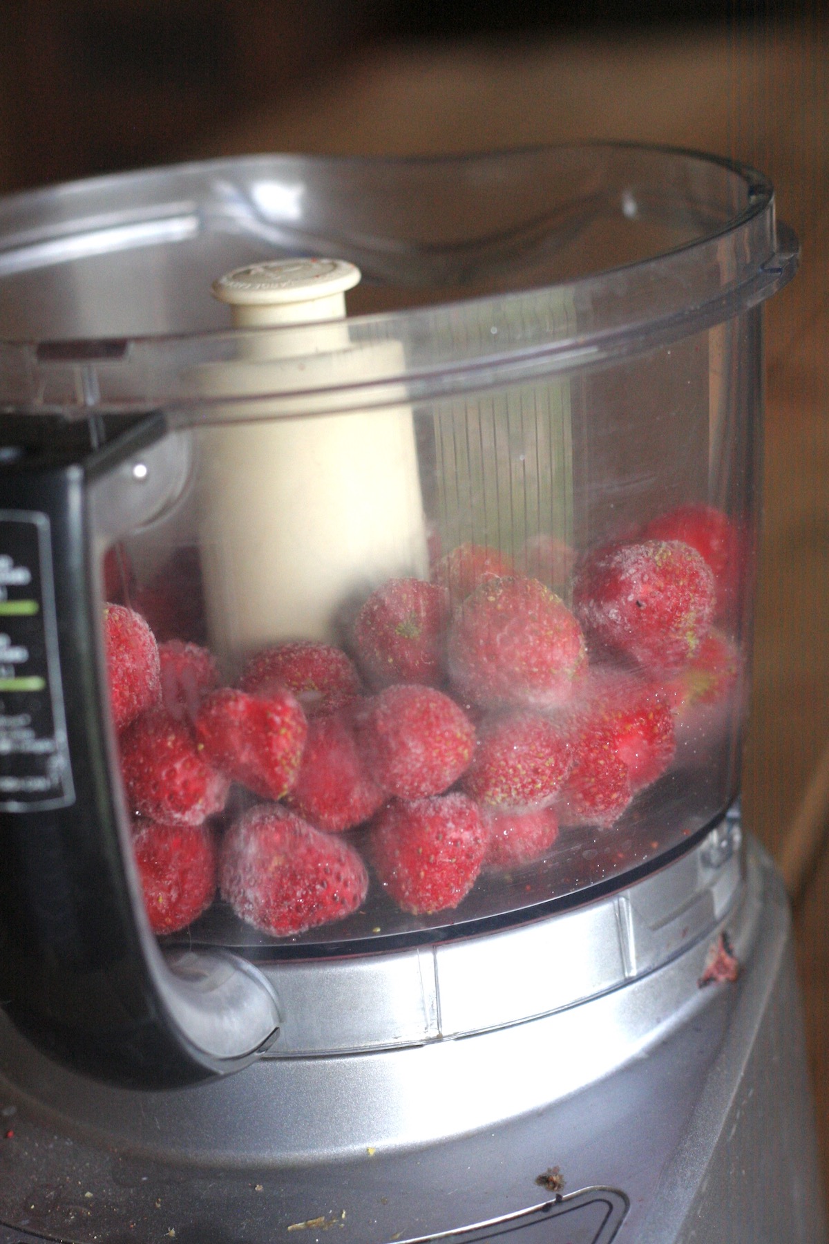 Whole frozen strawberries in the bowl of a food processor.