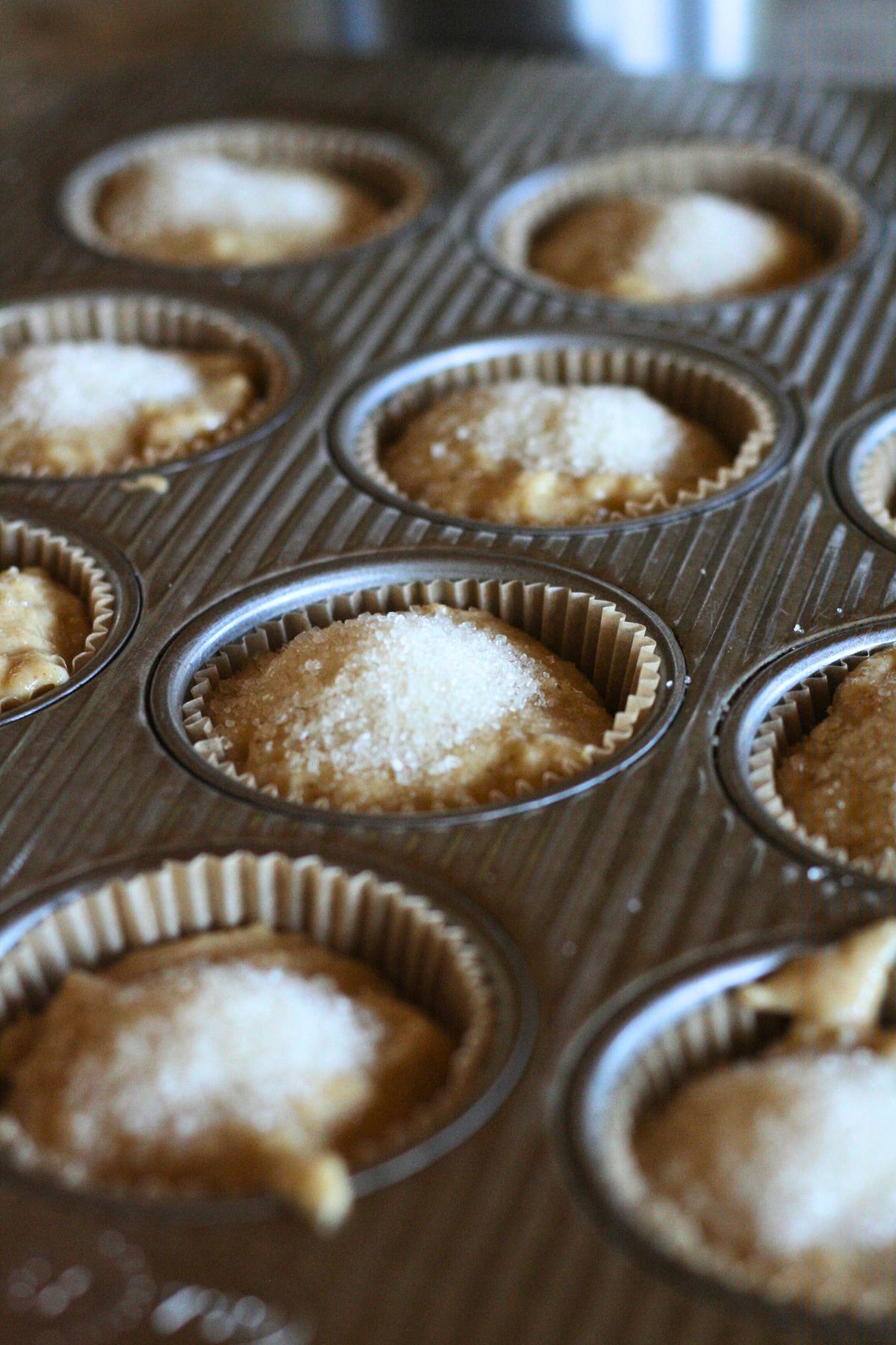 Coarse sugar on top of pumpkin muffin batter in a muffin tin.