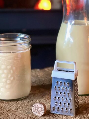 Raw egg nog in two jars next to a mini grater and whole nutmeg.