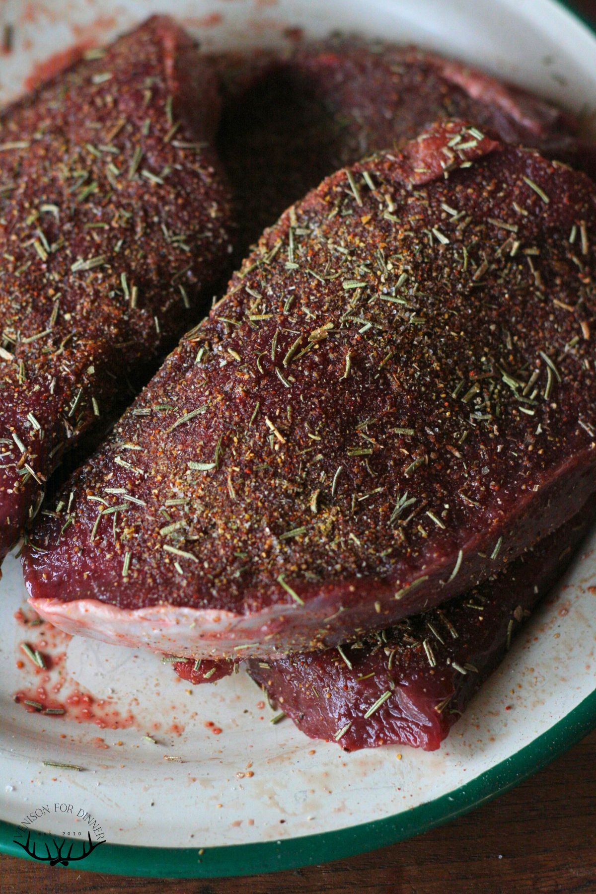 Raw moose steak with herbs on a platter.