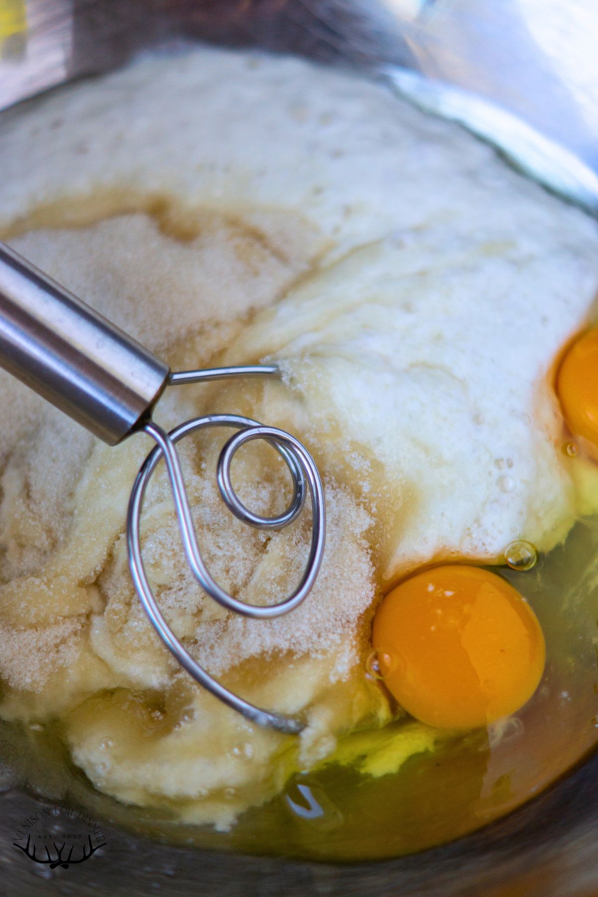A whisk with eggs in a mixing bowl.