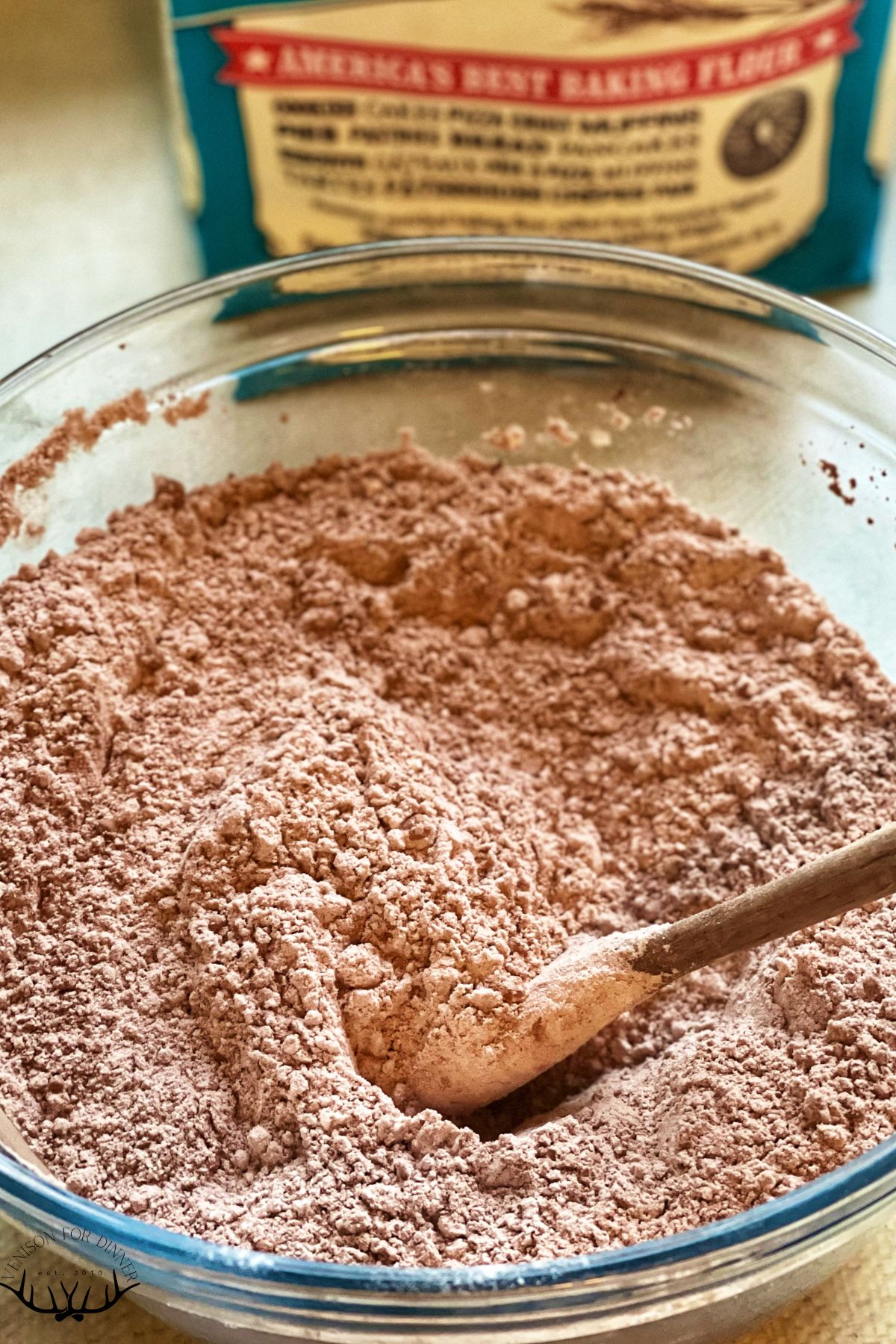 A wooden spoon in a bowl of flour and cocoa powder.