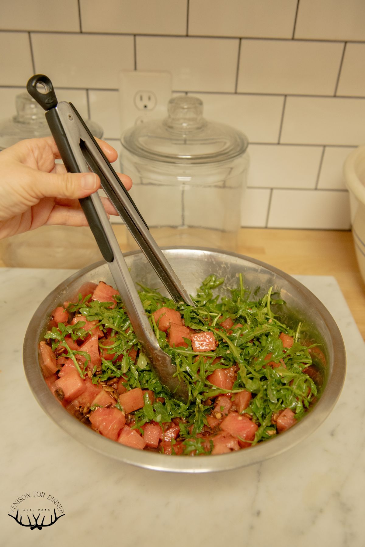 Tossing watermelon salad in a bowl.