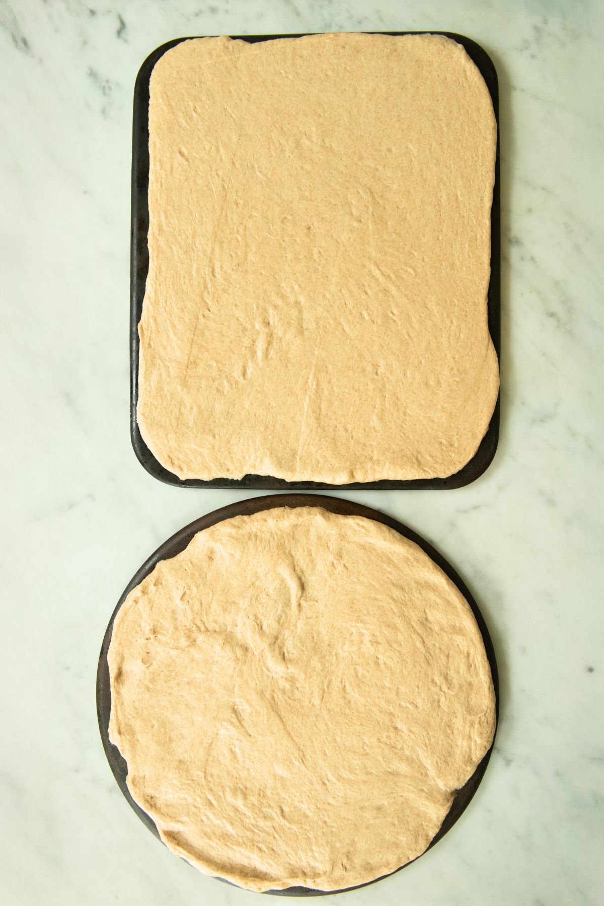 Whole wheat pizza dough rolled out in two pans.