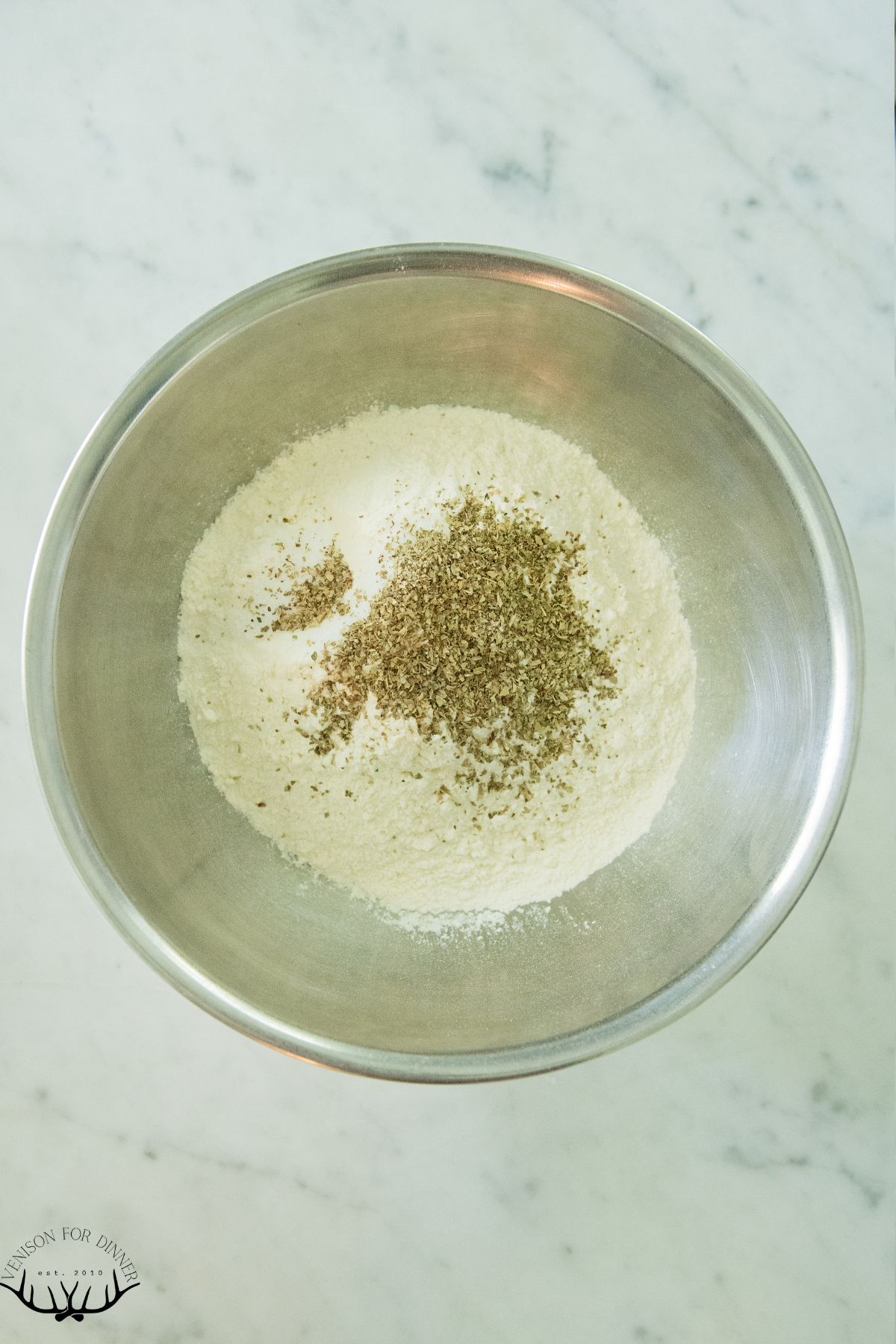 Flour and dried basil in a mixing bowl.