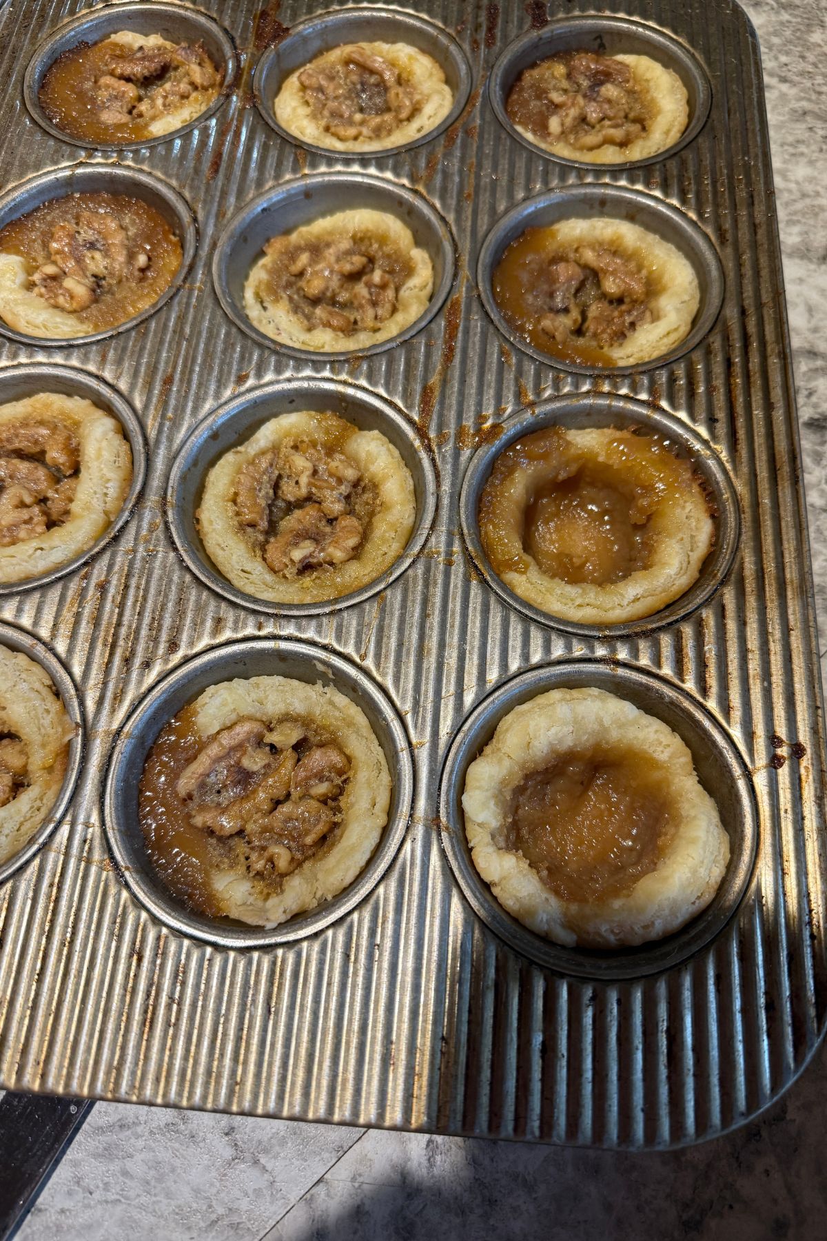 Baked butter tarts in a muffin tin.